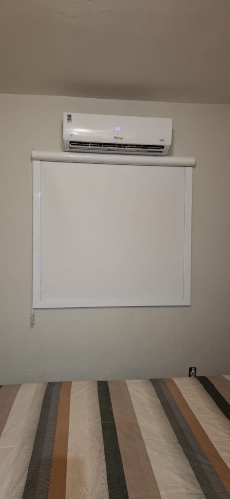 Persiana blackout branca instalada em quarto, abaixo de ar-condicionado